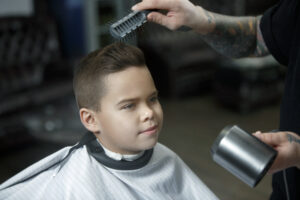 Children hairdresser cutting little boy against a dark background