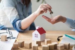 close-up-woman-s-hand-giving-house-key-man-wooden-table (1)