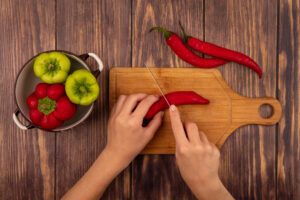 top-view-female-hands-cutting-chili-pepper-wooden-kitchen-board-with-knife-wooden-wall
